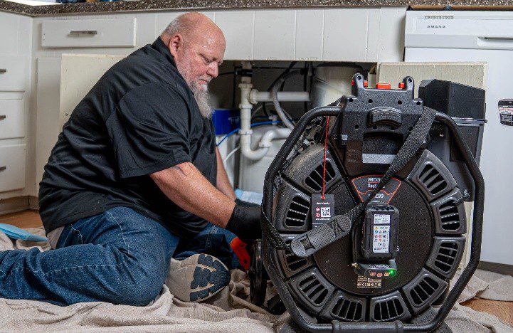 A professional plumber operating a drain cleaning machine beneath a kitchen sink to remove blockages and restore proper drainage.