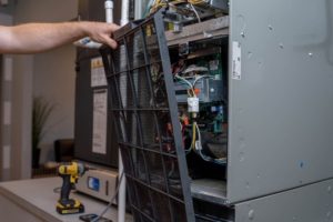 Technician removing the front panel from a furnace to access internal components.