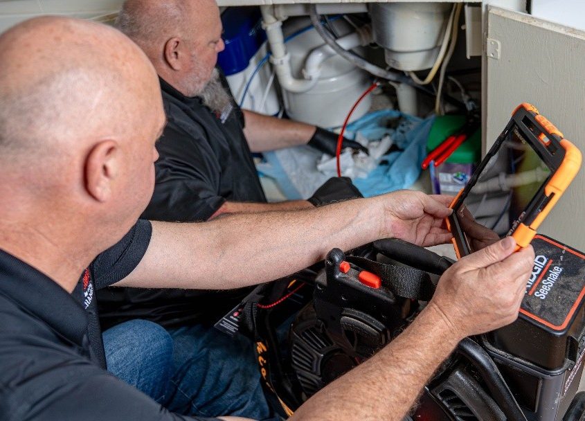 Plumbing technicians conducting leak detection under a kitchen sink with advanced camera equipment during a leak repair service in Lewisville, TX.