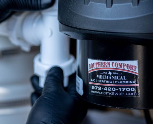 Plumbing technician adjusting a garbage disposal connection beneath a sink, showing the Southern Comfort Mechanical AC, heating, and plumbing label.