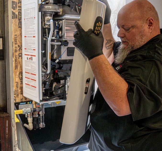 Professional plumber servicing a tankless water heater, removing the front access panel to inspect internal components.