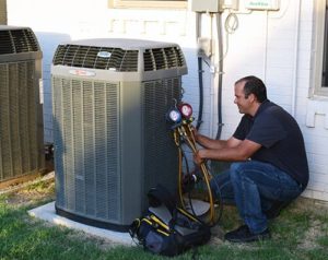 HVAC technician inspecting and servicing an outdoor heat pump unit with refrigerant gauges