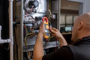 Professional HVAC technician using a clamp meter to diagnose electrical issues inside a central air conditioning system.